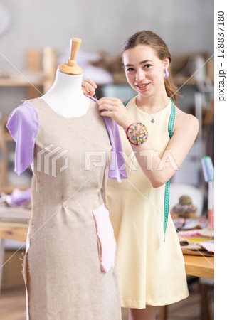 Female tailor sews new dress on a mannequin in sewing studio Female tailor sews new dress on a mannequin in sewing studio 128837180
