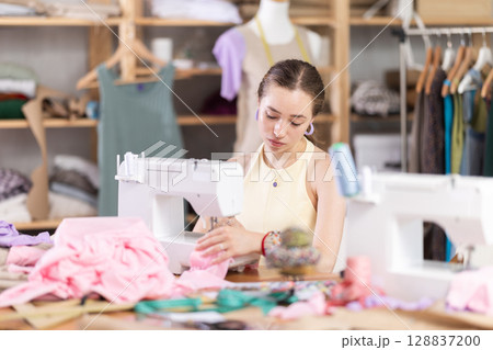 Woman seamstress sews on sewing machine in workshop Woman seamstress sews on sewing machine in workshop 128837200