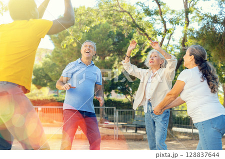 Joyful multiracial group of mature adult people playing volleyball game outdoors Joyful multiracial group of mature adult people playing volleyball game outdoors 128837644
