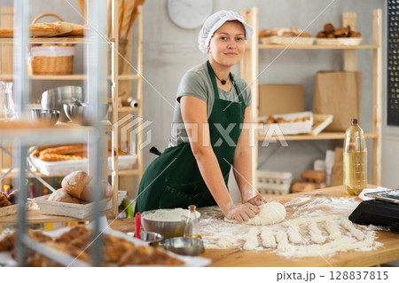 Woman works in bakery as baker, kneads dough, works with flour. 128837815