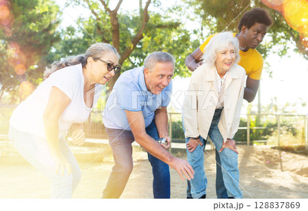 Cheerful males and females playing petanque in park on holidays Cheerful males and females playing petanque in park on holidays 128837869