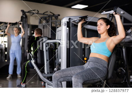 Girl performing shoulders press in exercise machine in gym Girl performing shoulders press in exercise machine in gym 128837977