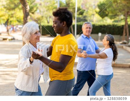 Carefree senior multiracial couples dancing in pairs outdoors during sunny day at park 128838039