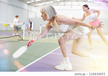 Aged woman playing friendly pickleball match on indoor court Aged woman playing friendly pickleball match on indoor court 128838055