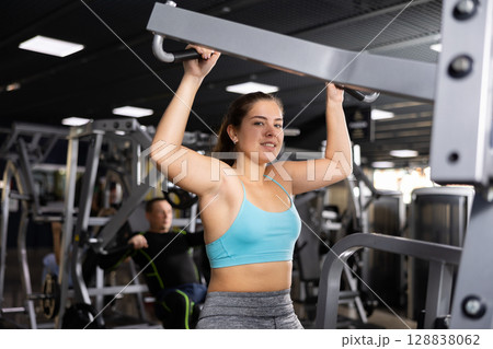 Young woman trains her arm muscles using a simulator in gym 128838062