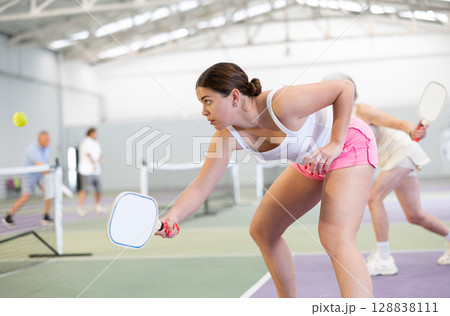 Young woman bouncing ball in pickleball game on court with racket Young woman bouncing ball in pickleball game on court with racket 128838111