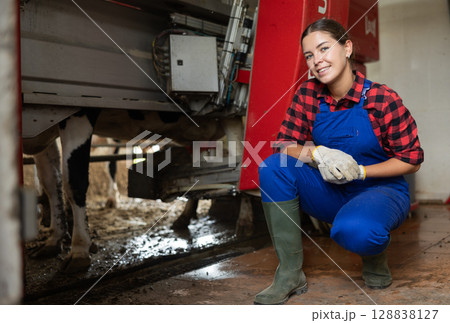Young girl pumps milk from cow, works and uses automatic milking machine. 128838127