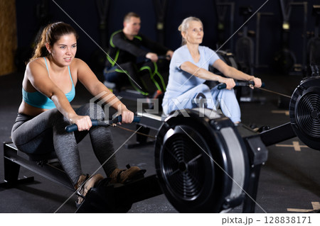 Young girl exercising on rowing machine during workout in gym 128838171