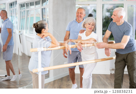 Active old attendees of ballet courses communicating cheerfully at ballet-barre 128838231