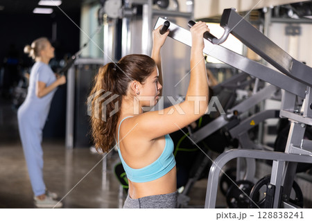Young female training trains the muscles of the arms and press on simulator in gym. Sport concept 128838241