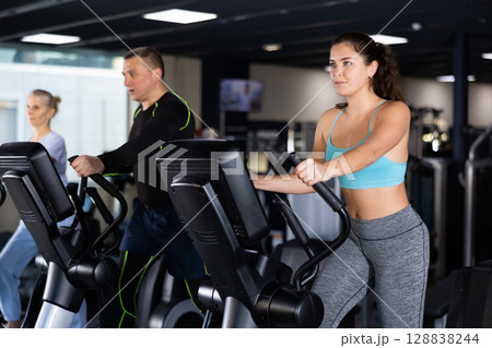 Athletic young woman exercising on an elliptical trainer in gym Athletic young woman exercising on an elliptical trainer in gym 128838244
