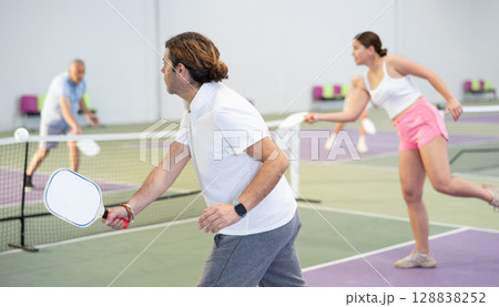 Rear view of adult man playing pickleball on indoor court Rear view of adult man playing pickleball on indoor court 128838252