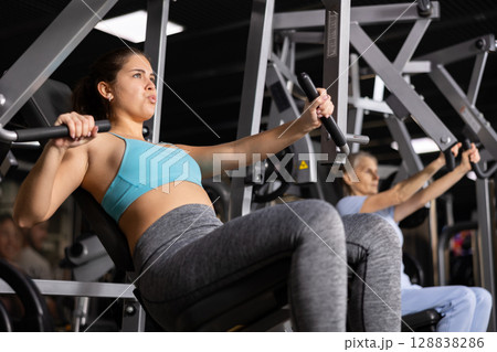 Active young woman training at chest press machine in gym Active young woman training at chest press machine in gym 128838286