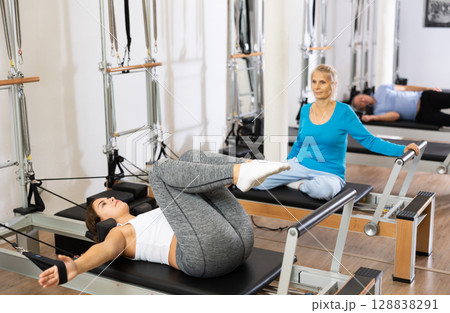 Positive calm young woman doing lower back exercises while lying on Pilates bed in wellness center 128838291