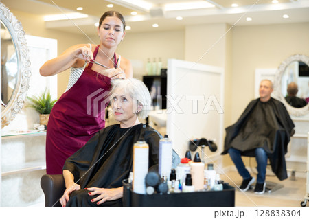 Young woman master completes creation of senior female clients image with help of scissors Young woman master completes creation of senior female clients image with help of scissors 128838304