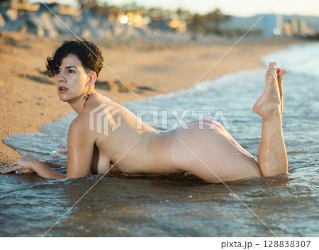Nude young adult woman lying on beach 128838307