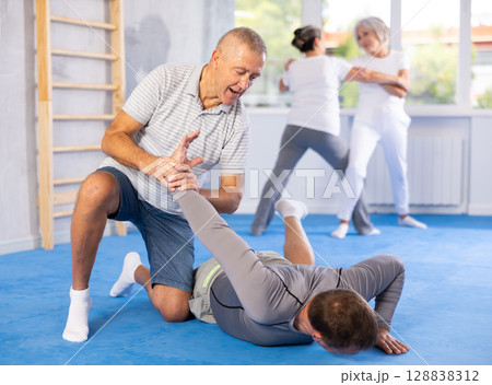 Old man twisting her opponent's arm during self-defense classes Old man twisting her opponent's arm during self-defense classes 128838312