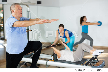 Aged man practicing pilates on pedal fitness chair in sports hall 128838500