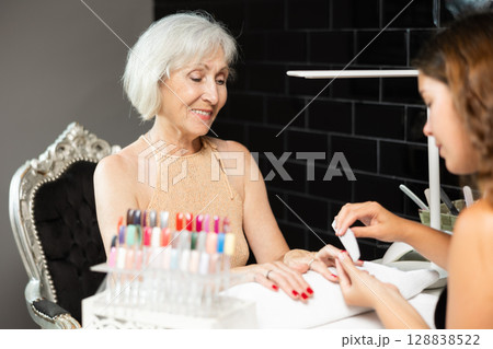 Smiling elderly woman receiving manicure from female manicurist in salon 128838522