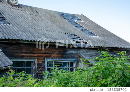 Dilapidated wooden house with damaged roof and overgrown garden symbolizing decay and abandonment Dilapidated wooden house with damaged roof and overgrown garden symbolizing decay and abandonment 128838702