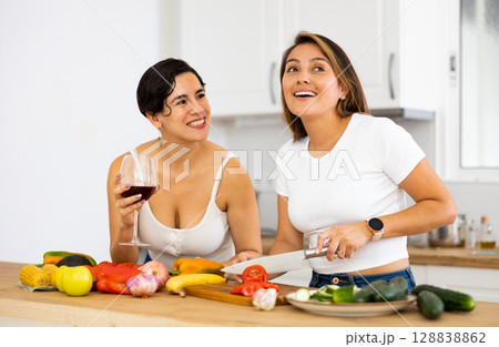 Smiling Hispanic women drinking wine and cooking in home kitchen 128838862