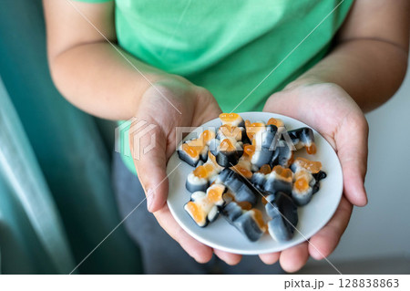 Child holding small plate of gummy candy in open hands 128838863