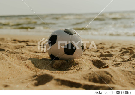 Soccer ball resting on sandy beach by ocean waves Soccer ball resting on sandy beach by ocean waves 128838865