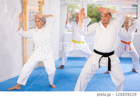 Middle-aged man attendee of karate classes practicing kata standing in row with others Middle-aged man attendee of karate classes practicing kata standing in row with others 128839229