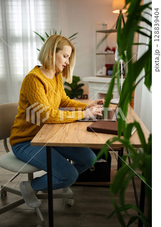 Focused professional in cozy home office working on laptop during a bright afternoon Focused professional in cozy home office working on laptop during a bright afternoon 128839404