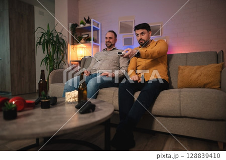 Friends enjoying a movie night at home, laughter and snacks fill the cozy living room atmosphere in the evening glow 128839410