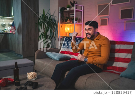 Excitement fills the room as a man celebrates during a game night with friends at home Excitement fills the room as a man celebrates during a game night with friends at home 128839417