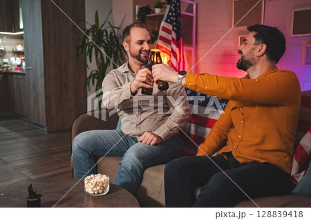 Friends enjoy a lively evening celebration with drinks and laughter in a cozy living room adorned with patriotic decor 128839418