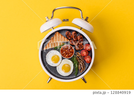 Breakfast of fried eggs with bacon or sausage and vegetables. ? plate on a vintage alarm clock Breakfast of fried eggs with bacon or sausage and vegetables. ? plate on a vintage alarm clock 128840919