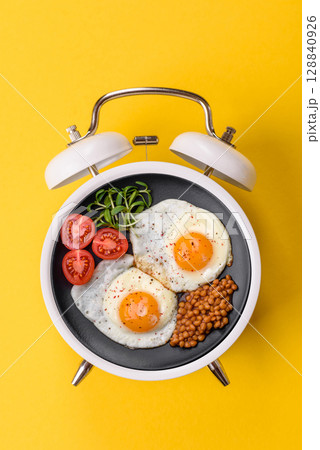 Breakfast of fried eggs with bacon or sausage and vegetables. ? plate on a vintage alarm clock 128840926