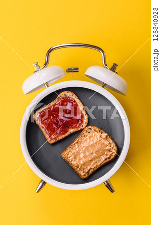 A breakfast of sandwiches with toast and peanut butter. Breakfast plate concept on a vintage alarm clock A breakfast of sandwiches with toast and peanut butter. Breakfast plate concept on a vintage alarm clock 128840928