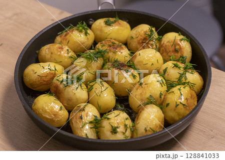 Young jacket potatoes fried in a frying pan and sprinkled with herbs 128841033