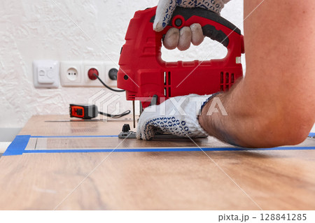 repairman with electric jigsaw doing sawing place for installing hob in a worktop in the kitchen, close-up repairman with electric jigsaw doing sawing place for installing hob in a worktop in the kitchen, close-up 128841285