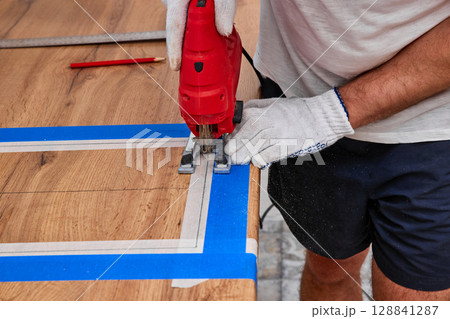repairman with electric jigsaw doing sawing place for installing hob in a worktop in the kitchen repairman with electric jigsaw doing sawing place for installing hob in a worktop in the kitchen 128841287