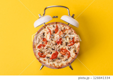 Time to eat Italian pizza cut in slices. Concept in the form of pizza on a vintage alarm clock 128841334
