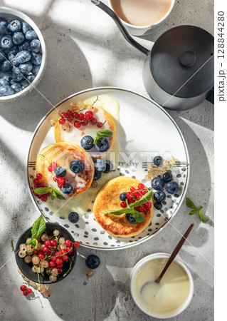 Cottage cheese pancakes with berries and condensed milk top view. Homemade dessert syrniki for healthy breakfast, bright morning light 128844280