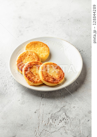 Cottage cheese pancakes on a plate on light background isolated. Homemade dessert syrniki for healthy breakfast, text space Cottage cheese pancakes on a plate on light background isolated. Homemade dessert syrniki for healthy breakfast, text space 128844289