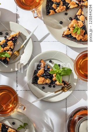 A slice of homemade blueberry crumble pie on a plate on white tile background top view. Sweet breakfast composition in bright morning light A slice of homemade blueberry crumble pie on a plate on white tile background top view. Sweet breakfast composition in bright morning light 128844294