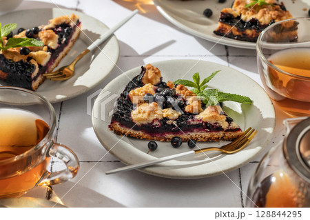 A slice of homemade blueberry crumble pie on a plate on white tile background. Sweet breakfast composition in bright morning light 128844295