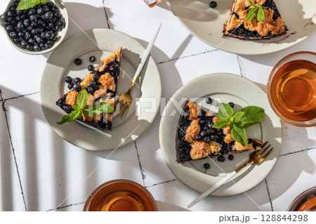 Slices of homemade blueberry crumble pie on plates on white tile background top view. Sweet breakfast composition in bright morning light 128844298