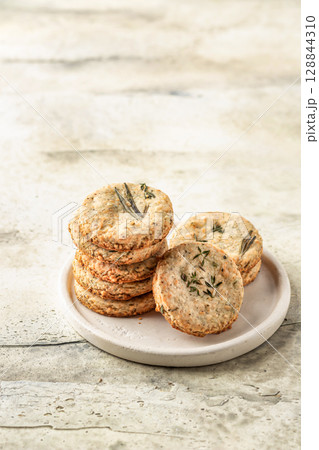 Shortbread cheese cookies with aromatic herbs on white plate on rustic textured background isolated. Savory parmesan cookies for party Shortbread cheese cookies with aromatic herbs on white plate on rustic textured background isolated. Savory parmesan cookies for party 128844310