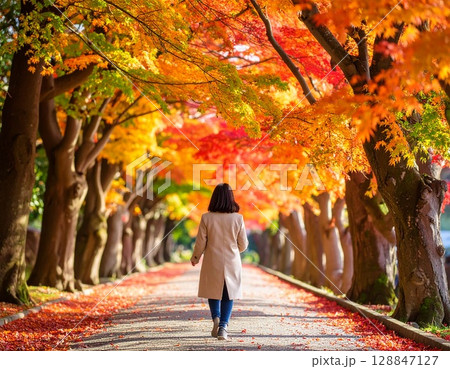 紅葉する並木道を歩く女性 128847127