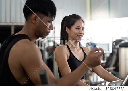Trainer assisting young woman during gym workout 128847282