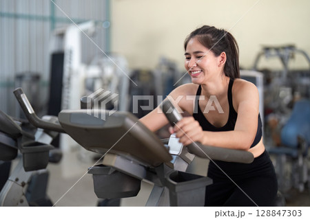 Young woman enjoying workout on exercise bike with trainer Young woman enjoying workout on exercise bike with trainer 128847303