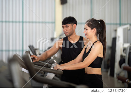 Trainer and woman engaging in workout at gym equipment 128847304