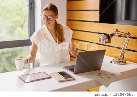 A modern workspace with a professional woman multitasking on devices, focused on productivity A modern workspace with a professional woman multitasking on devices, focused on productivity 128847663